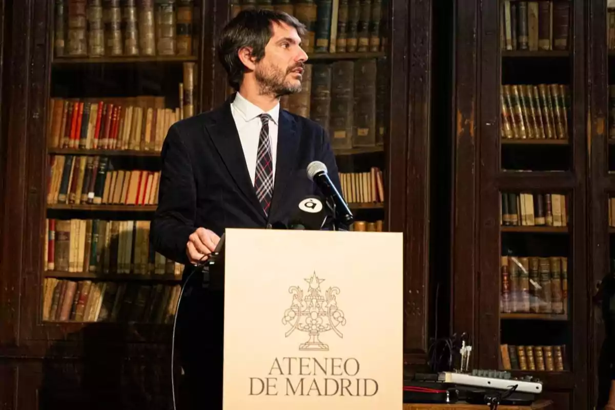 Un hombre hablando en un podio en el Ateneo de Madrid con estanterías llenas de libros al fondo.