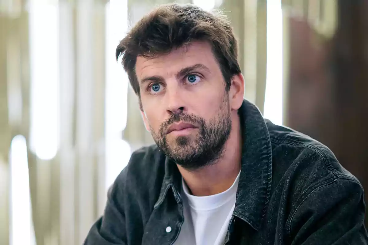Gerard Piqué mira pensativamente hacia adelante, vistiendo una chaqueta oscura sobre una camiseta blanca, con un fondo desenfocado. Gerard Piqué mira pensativamente hacia adelante, vistiendo una chaqueta oscura sobre una camiseta blanca, con un fondo desenfocado.