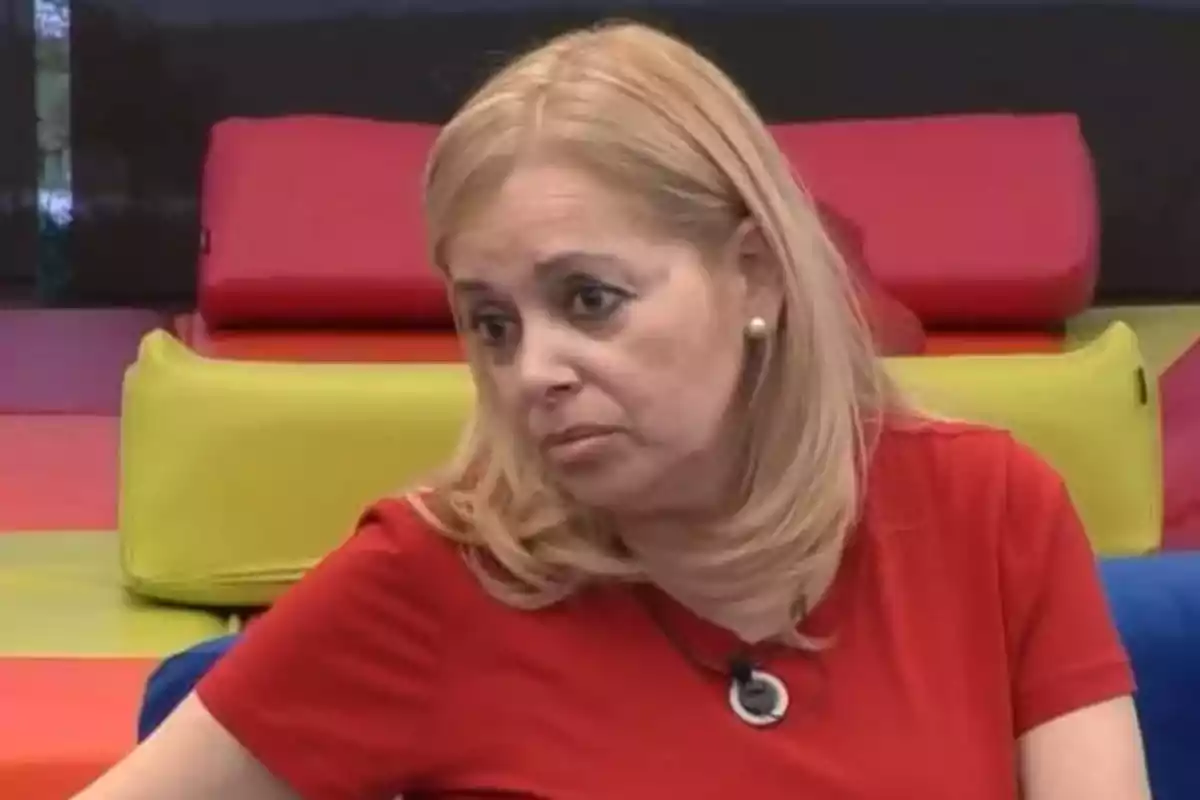 Emma Ozores con expresión seria lleva una camiseta roja y está sentada frente a un fondo de cojines de colores brillantes. Emma Ozores con expresión seria lleva una camiseta roja y está sentada frente a un fondo de cojines de colores brillantes.