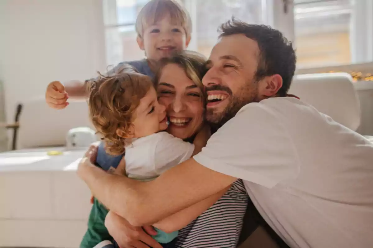 Una familia sonriente abrazándose en una sala iluminada por la luz del día.