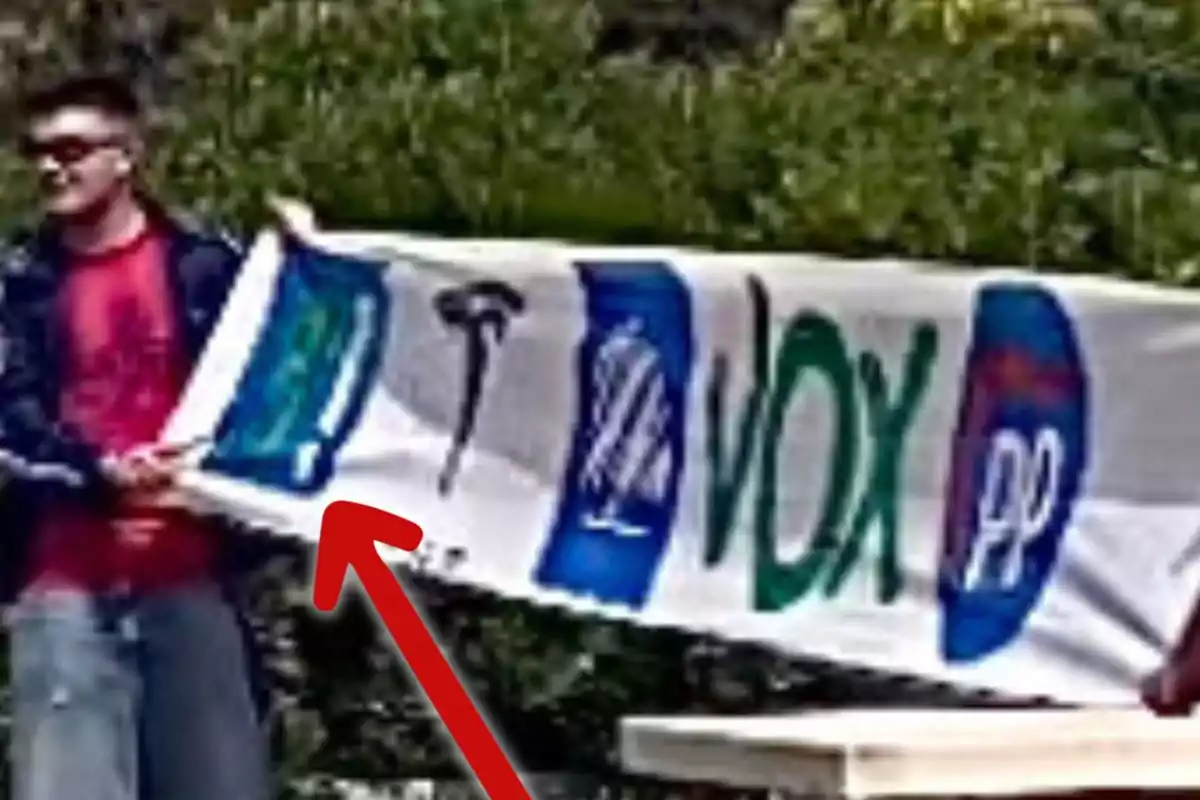 Un hombre sostiene una pancarta con logotipos de partidos políticos y un símbolo de martillo en un entorno al aire libre. Un hombre sostiene una pancarta con logotipos de partidos políticos y un símbolo de martillo en un entorno al aire libre.