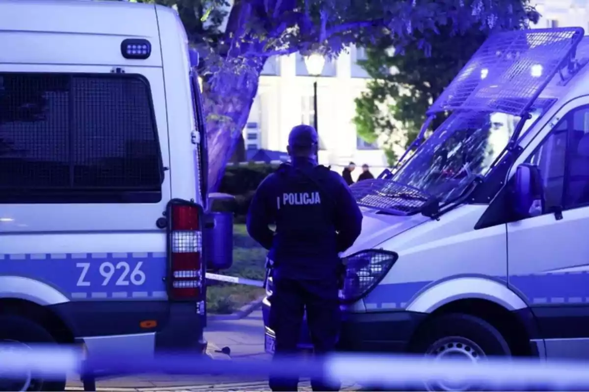 Un oficial de policía de pie entre dos vehículos policiales en una escena iluminada con luces azules. Un oficial de policía de pie entre dos vehículos policiales en una escena iluminada con luces azules.