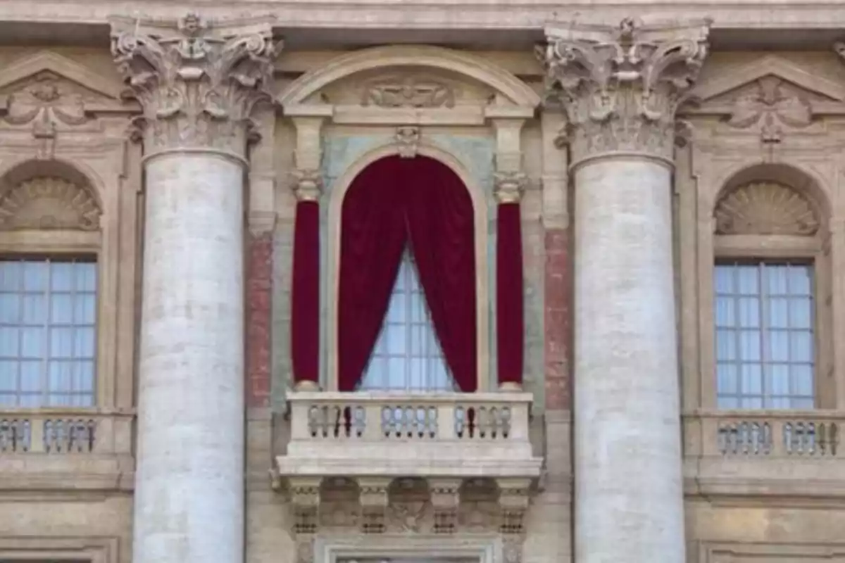 Fachada de un edificio con columnas y un balcón adornado con cortinas rojas.