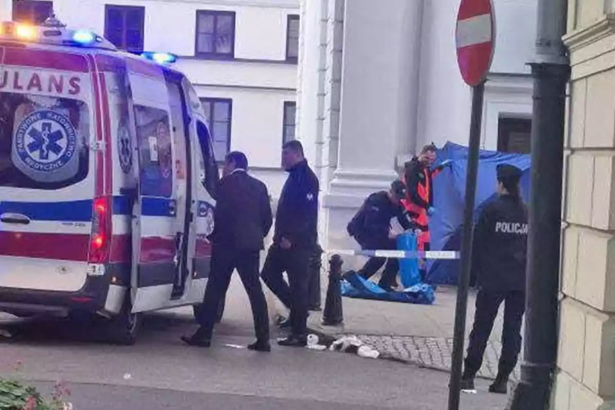 Una ambulancia y varios oficiales de policía están presentes en una escena acordonada en la calle, donde se observa actividad de emergencia.