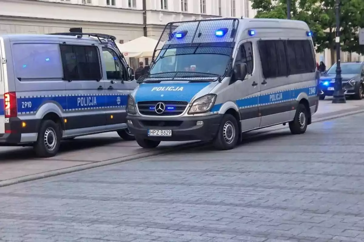 Dos furgonetas de policía con luces azules encendidas estacionadas en una calle pavimentada. Dos furgonetas de policía con luces azules encendidas estacionadas en una calle pavimentada.