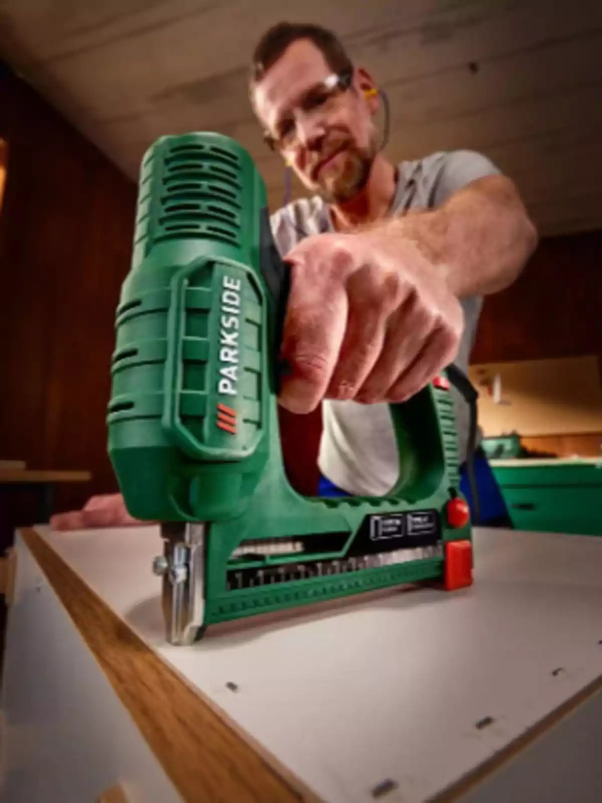 Persona usando una grapadora eléctrica verde para ensamblar un mueble de madera en un taller. Persona usando una grapadora eléctrica verde para ensamblar un mueble de madera en un taller.