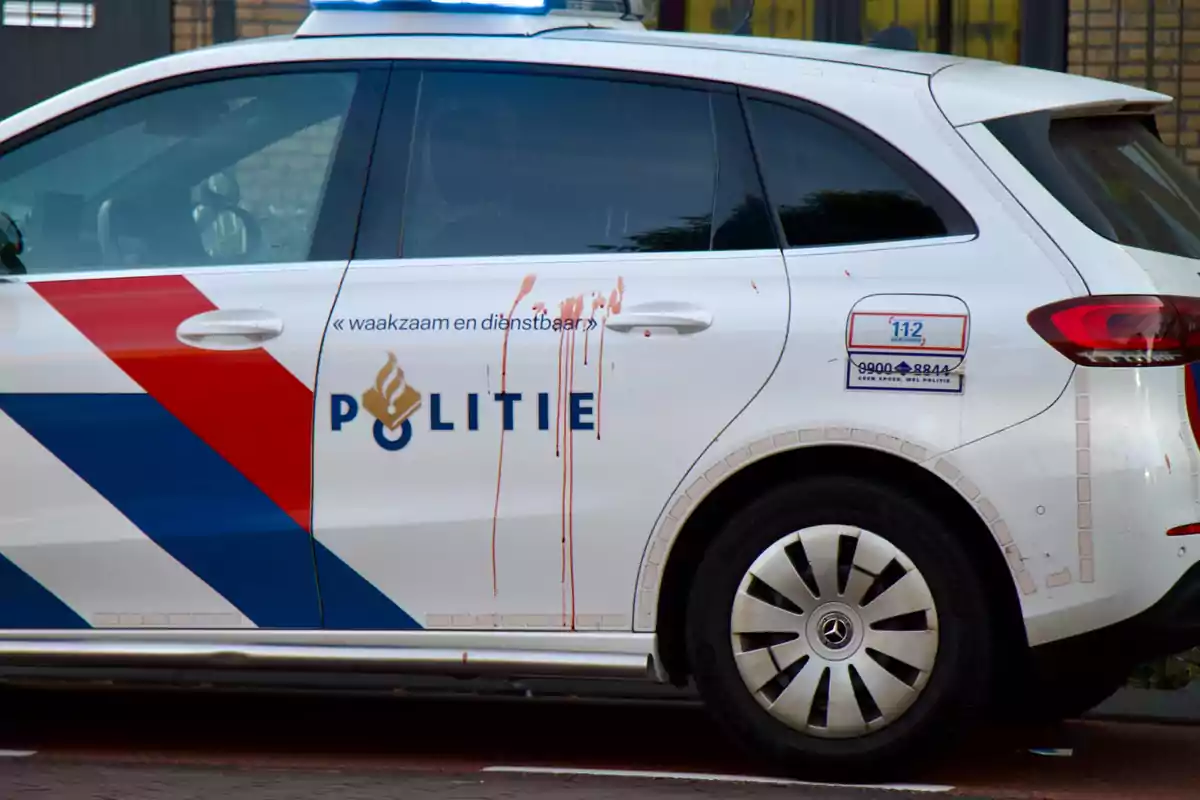 Un coche de policía con manchas rojas en la puerta lateral, con el texto "POLITIE" y un diseño de franjas rojas y azules.