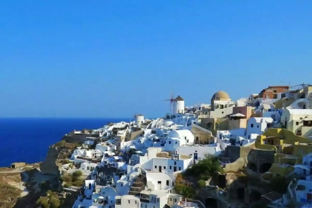 Vista panorámica de un pueblo costero con casas blancas y techos azules en una colina junto al mar.