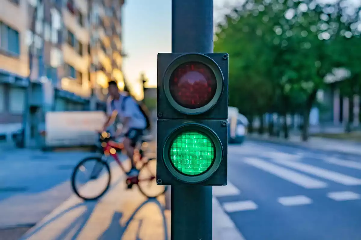 Semáforo en verde con un ciclista cruzando la calle en una ciudad al atardecer
