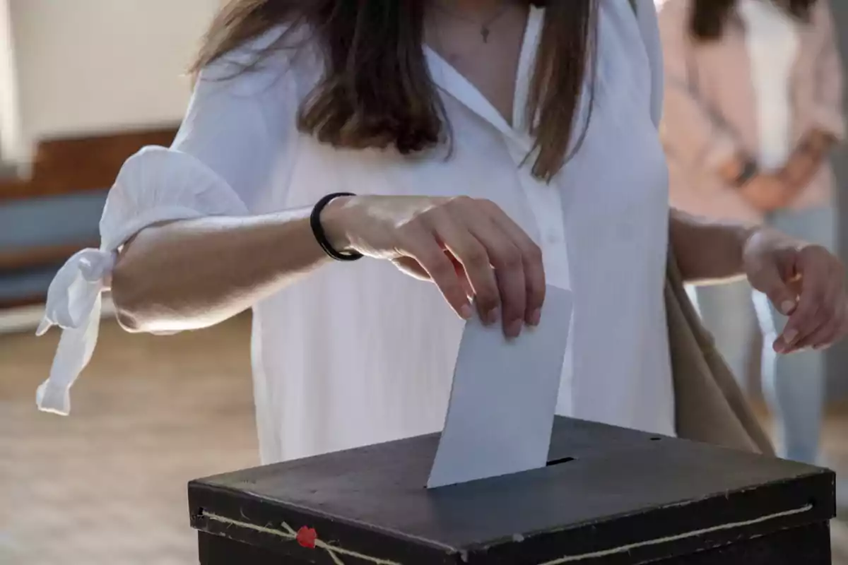 Persona depositando un sobre en una urna de votación.