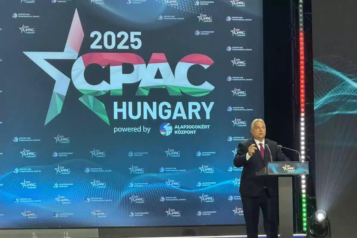 Un hombre de traje da un discurso en un podio frente a una pantalla grande que muestra el logo de CPAC 2025 Hungary Un hombre de traje da un discurso en un podio frente a una pantalla grande que muestra el logo de CPAC 2025 Hungary