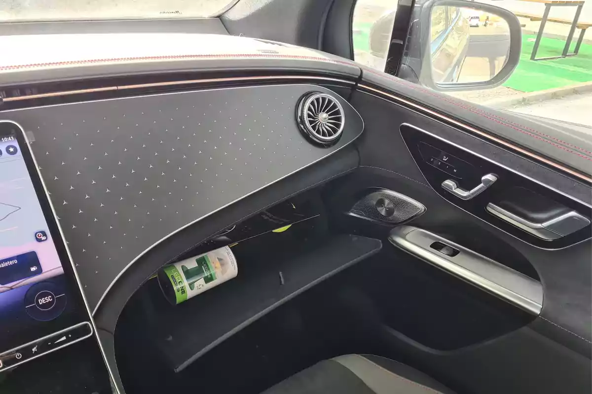 Interior de un automóvil moderno con un diseño elegante, que muestra la consola central, la guantera abierta con una lata en su interior, y el panel de la puerta del pasajero con controles y altavoces.