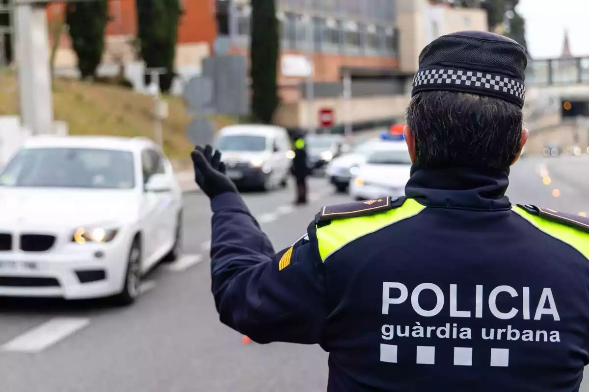 Plano corto de un agente de la Guardia Urbana de espaldas con una mano en alto Plano corto de un agente de la Guardia Urbana de espaldas con una mano en alto