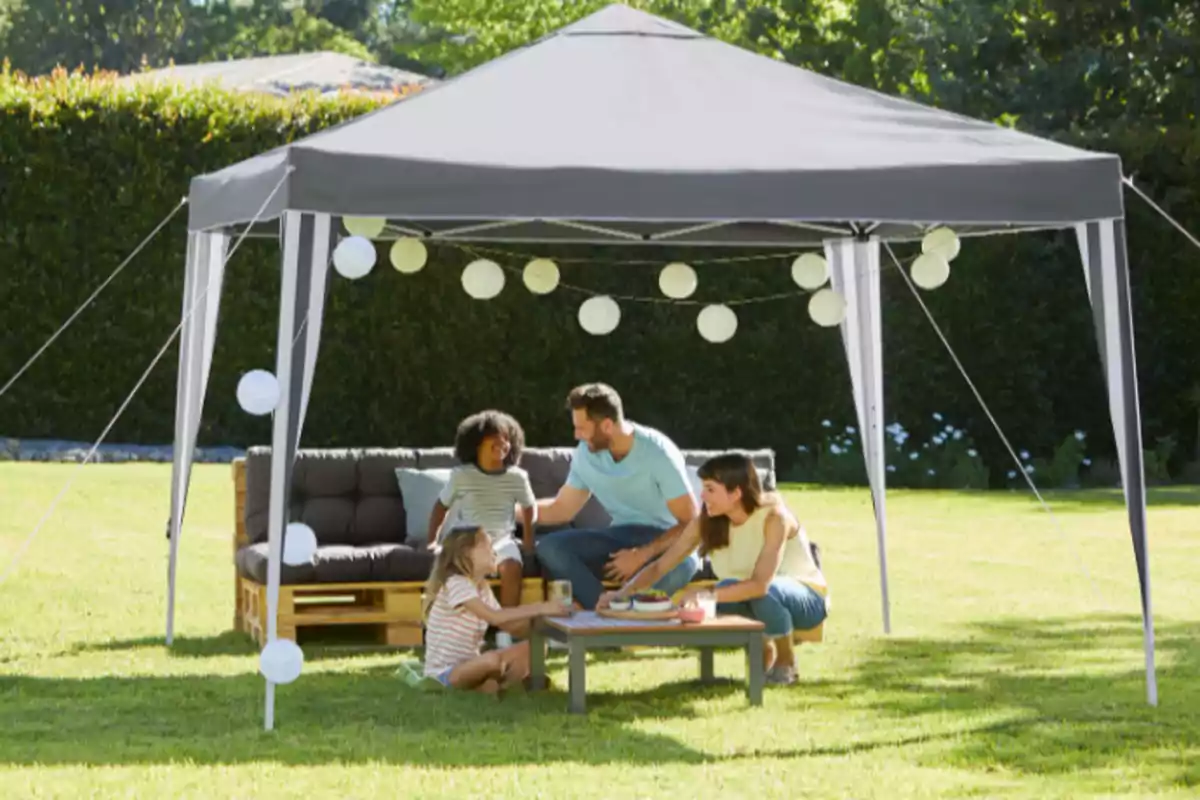 Una familia disfruta de un picnic bajo una carpa en un jardín, con luces decorativas colgando. Una familia disfruta de un picnic bajo una carpa en un jardín, con luces decorativas colgando.