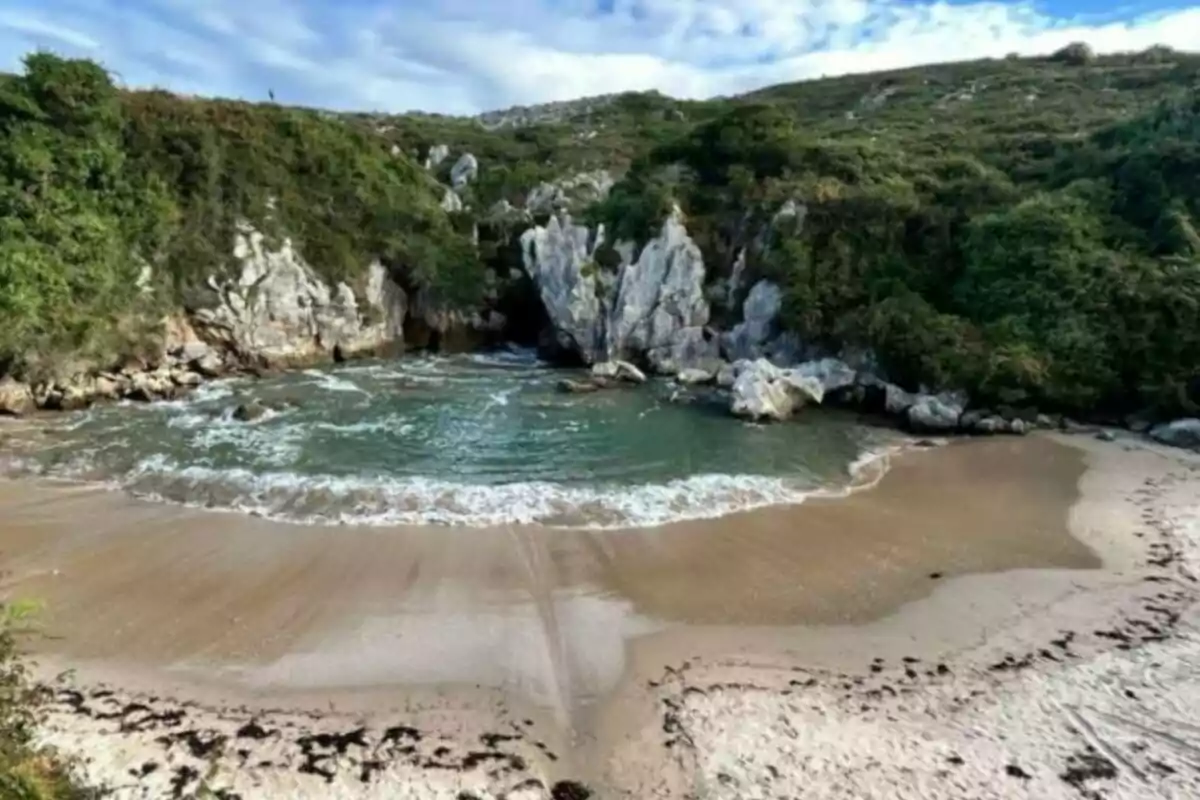 Una pequeña playa rodeada de acantilados y vegetación con aguas tranquilas y arena dorada.