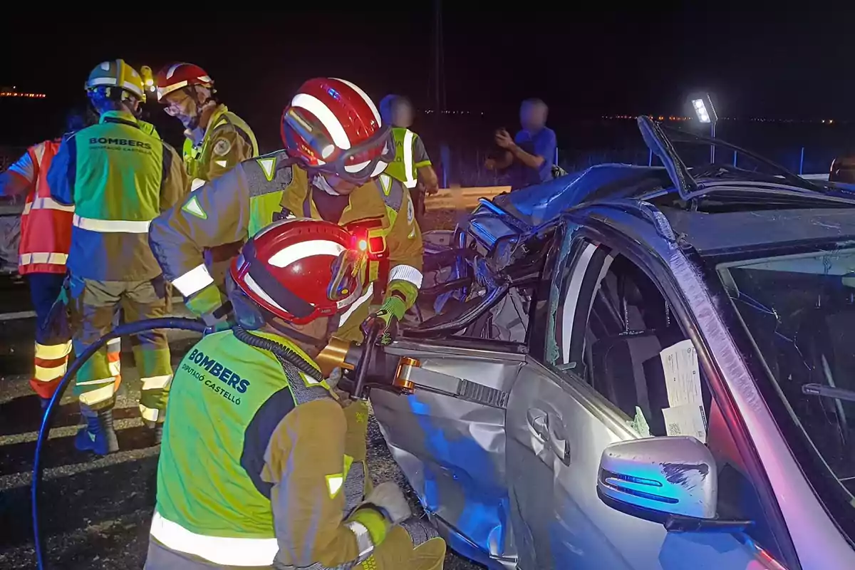 Bomberos trabajando en la escena de un accidente automovilístico por la noche.