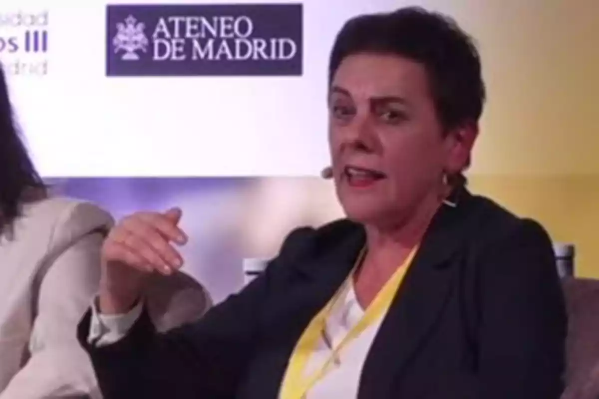 Mujer hablando en un evento con logos de la Universidad Carlos III y Ateneo de Madrid al fondo.