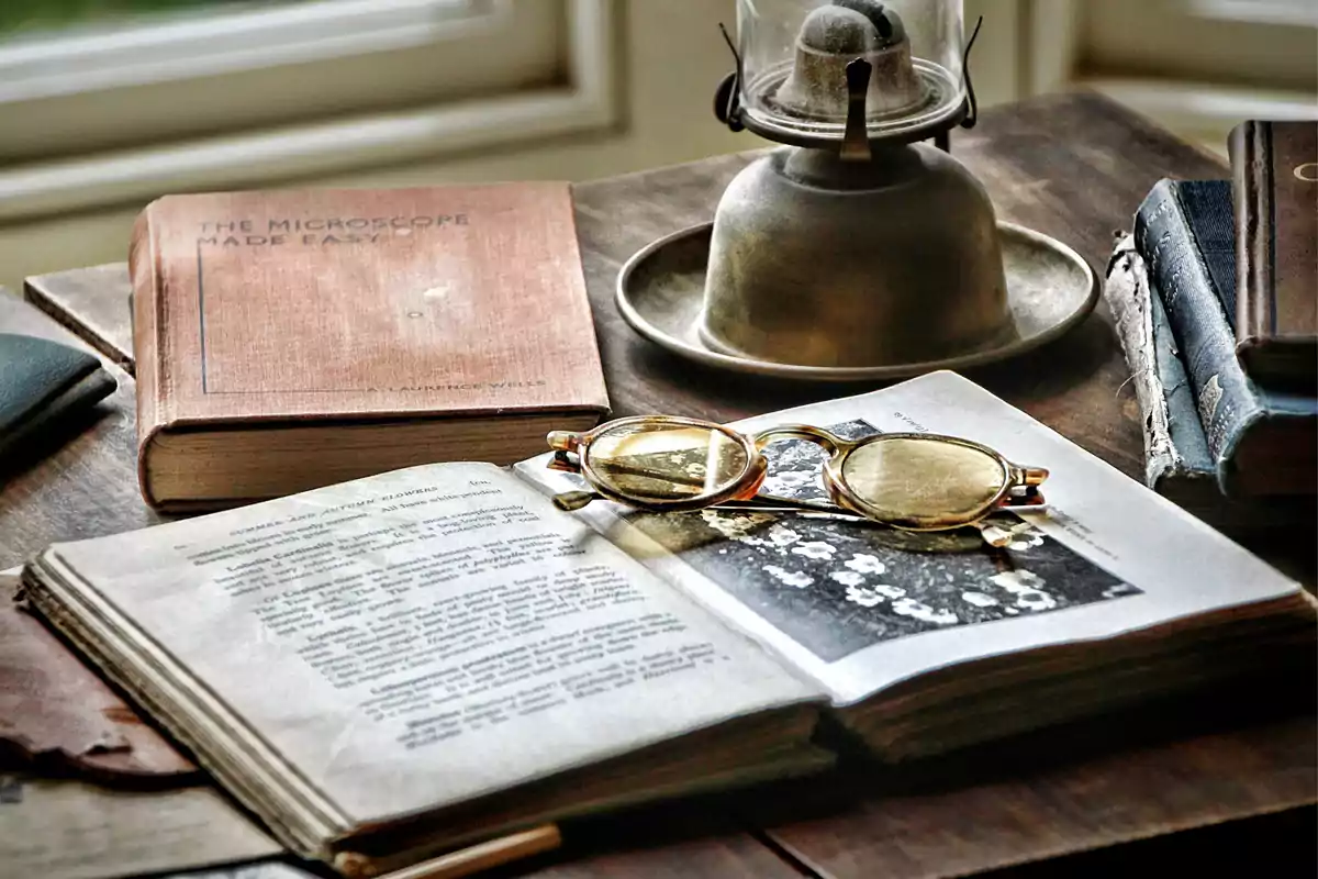 Un par de libros antiguos, unas gafas y una lámpara de aceite sobre una mesa de madera.