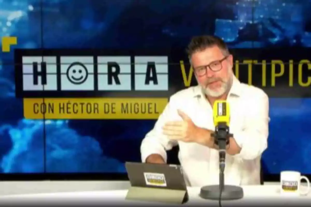 Un hombre con barba y gafas está sentado en un estudio de grabación, hablando frente a un micrófono amarillo con una pantalla detrás que muestra el título "HORA VENTIPICO CON HÉCTOR DE MIGUEL".