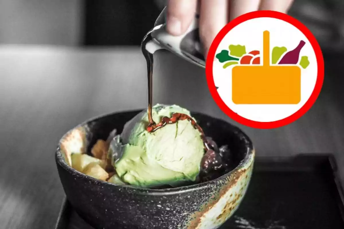 Una mano vertiendo un líquido oscuro sobre una bola de helado verde en un tazón negro con un icono de cesta de alimentos en la esquina superior derecha. Una mano vertiendo un líquido oscuro sobre una bola de helado verde en un tazón negro con un icono de cesta de alimentos en la esquina superior derecha.