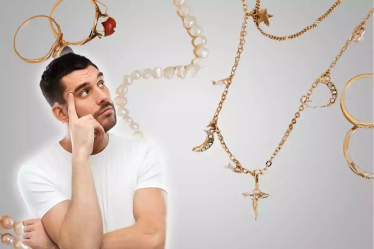 Hombre pensativo con camiseta blanca rodeado de joyas doradas y perlas sobre un fondo gris.