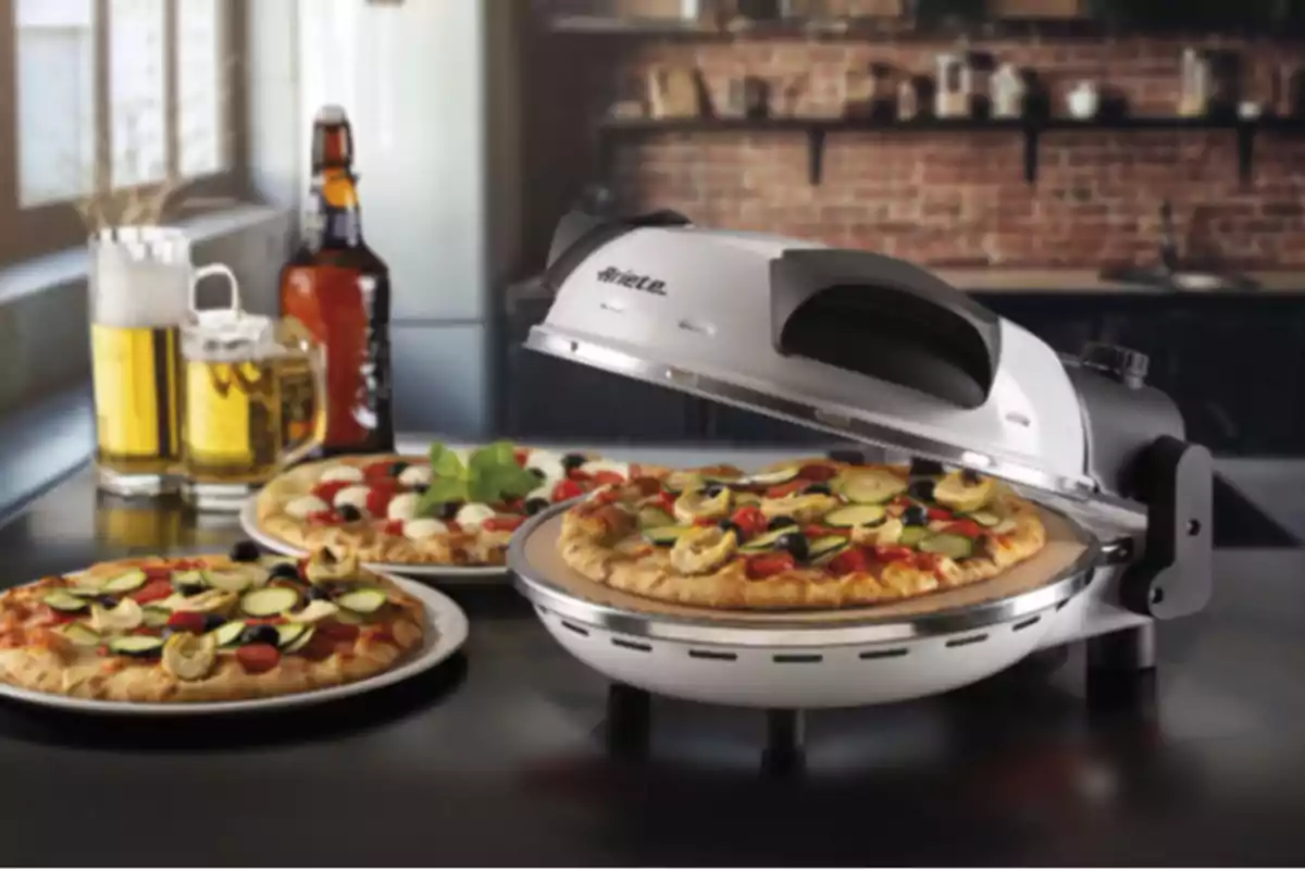 Una máquina para hacer pizzas con una pizza recién horneada y otra pizza en un plato al lado, acompañadas de una jarra de cerveza y una botella en una cocina moderna. Una máquina para hacer pizzas con una pizza recién horneada y otra pizza en un plato al lado, acompañadas de una jarra de cerveza y una botella en una cocina moderna.