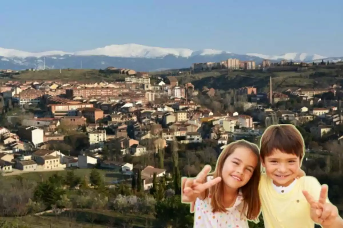 Dos niños posando frente a un paisaje urbano con montañas nevadas al fondo.