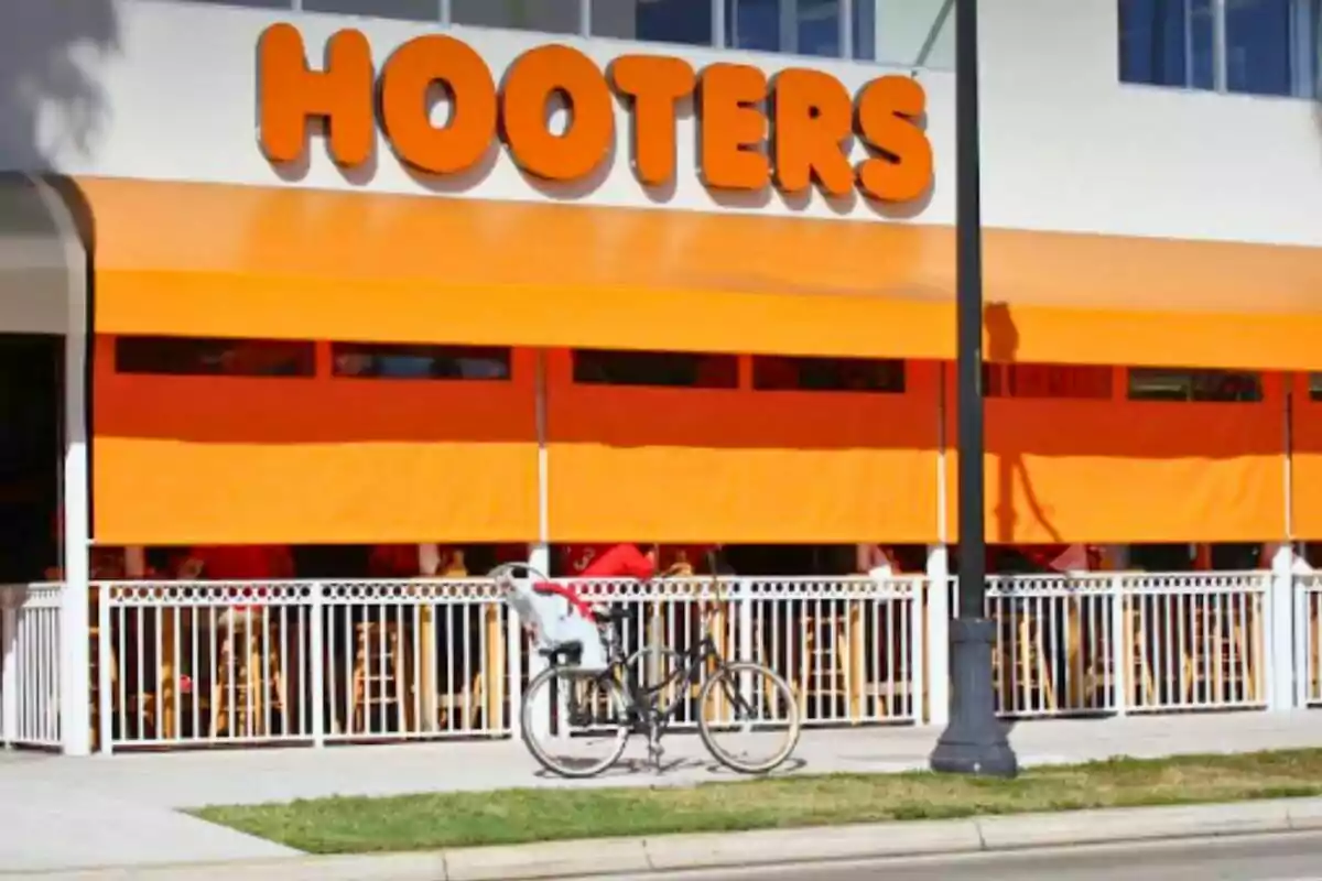 Facade of a Hooters restaurant with orange awnings and a bicycle parked on the sidewalk Facade of a Hooters restaurant with orange awnings and a bicycle parked on the sidewalk