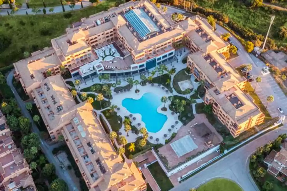 Aerial view of a residential complex with a central swimming pool and buildings surrounded by green areas.