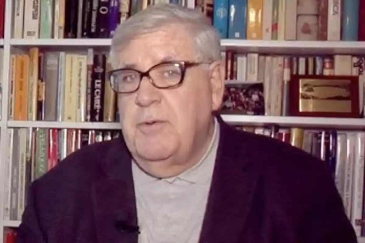 Un hombre con gafas y cabello canoso está frente a una estantería llena de libros.