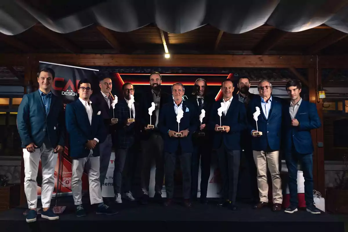 Un grupo de hombres posando en un escenario, algunos sosteniendo trofeos, con un fondo de madera y un cartel de diseño.