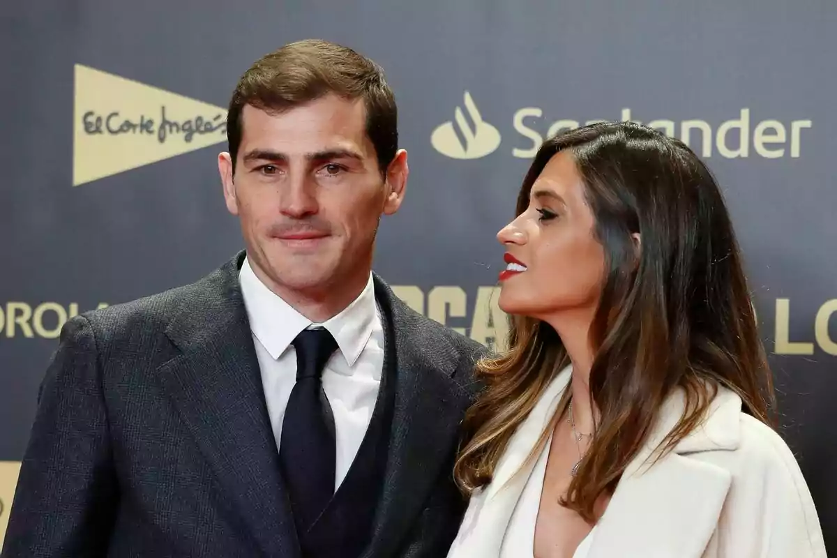 Iker Casillas y Sara Carbonero posando en un evento formal con fondo de logotipos de marcas. Iker Casillas y Sara Carbonero posando en un evento formal con fondo de logotipos de marcas.