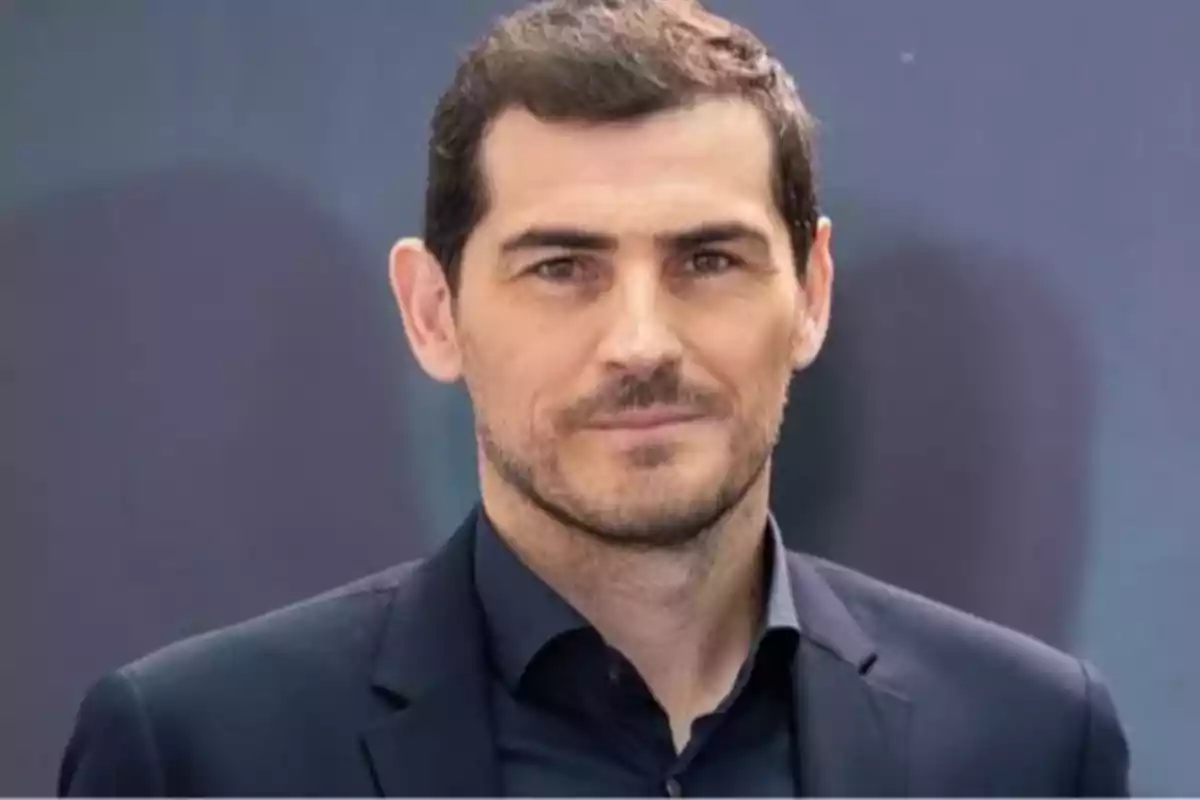 Hombre de cabello corto y barba ligera vistiendo un saco oscuro y camisa negra con fondo gris desenfocado Hombre de cabello corto y barba ligera vistiendo un saco oscuro y camisa negra con fondo gris desenfocado