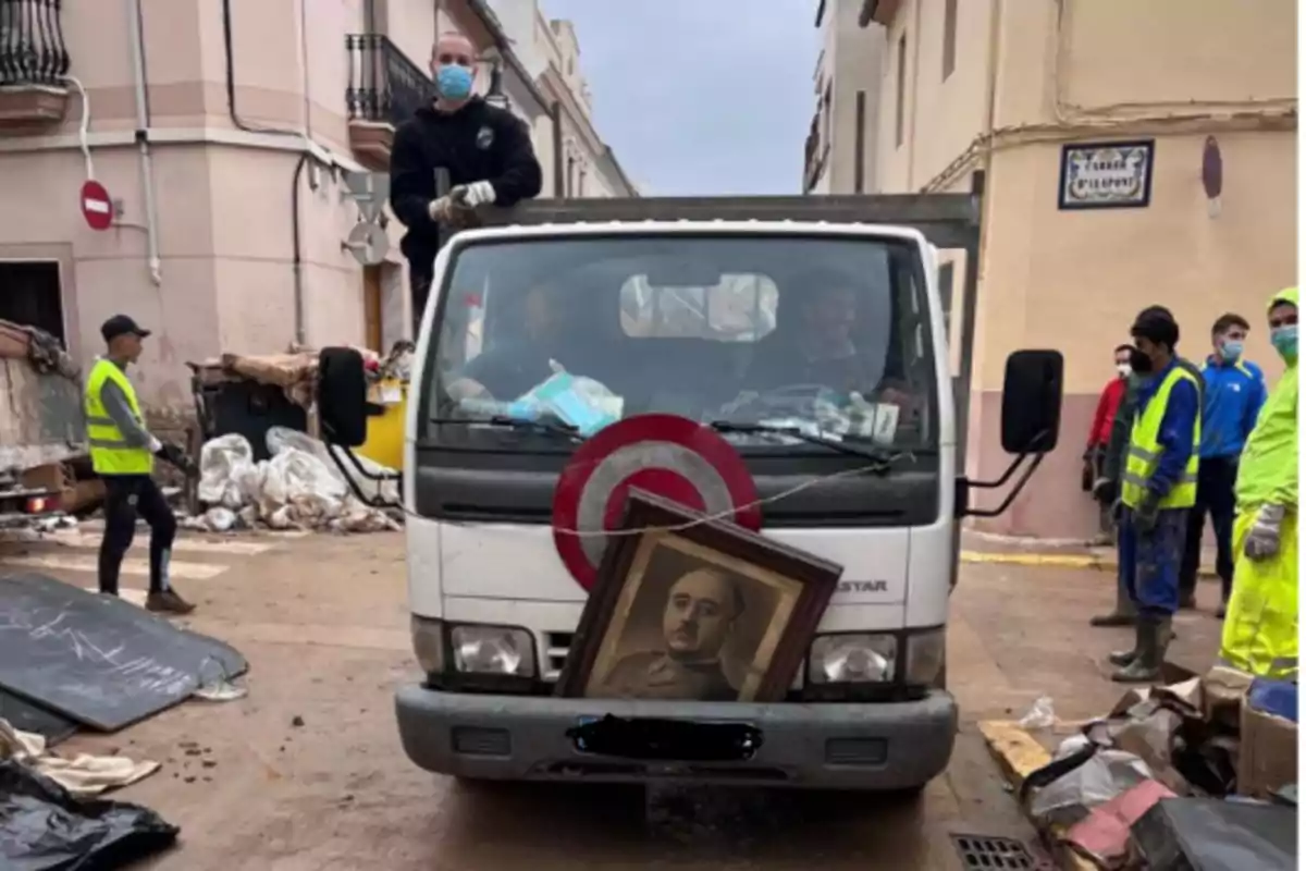 Un camión de limpieza en una calle con trabajadores alrededor y un retrato en la parte delantera del vehículo.