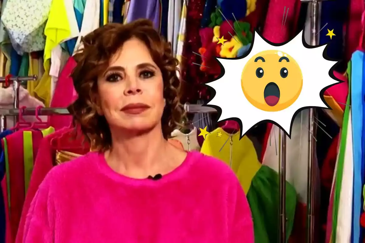 Ágatha Ruiz de la Prada con un suéter rosa está frente a un fondo colorido de ropa, junto a un emoji sorprendido.