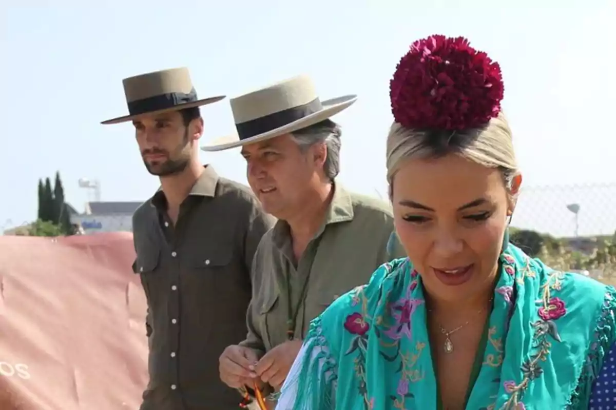 Tres personas vestidas con trajes típicos andaluces, dos hombres con sombrero de ala ancha y una mujer con mantón turquesa bordado y una flor roja en el cabello, en un ambiente al aire libre y soleado Tres personas vestidas con trajes típicos andaluces, dos hombres con sombrero de ala ancha y una mujer con mantón turquesa bordado y una flor roja en el cabello, en un ambiente al aire libre y soleado