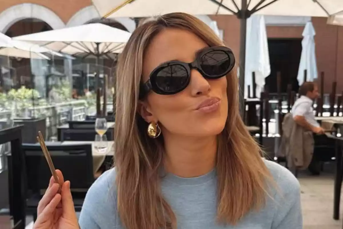 Alice Campello con gafas de sol negras y cabello rubio sonríe mientras está sentada en una terraza al aire libre Alice Campello con gafas de sol negras y cabello rubio sonríe mientras está sentada en una terraza al aire libre