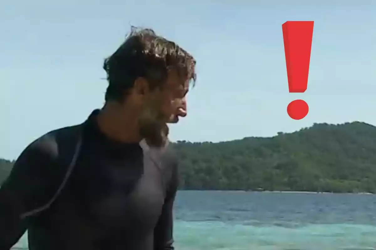 Álvaro Muñoz Escassi con barba mirando hacia la derecha en la orilla del mar con un gran signo de exclamación rojo sobre el fondo de una isla