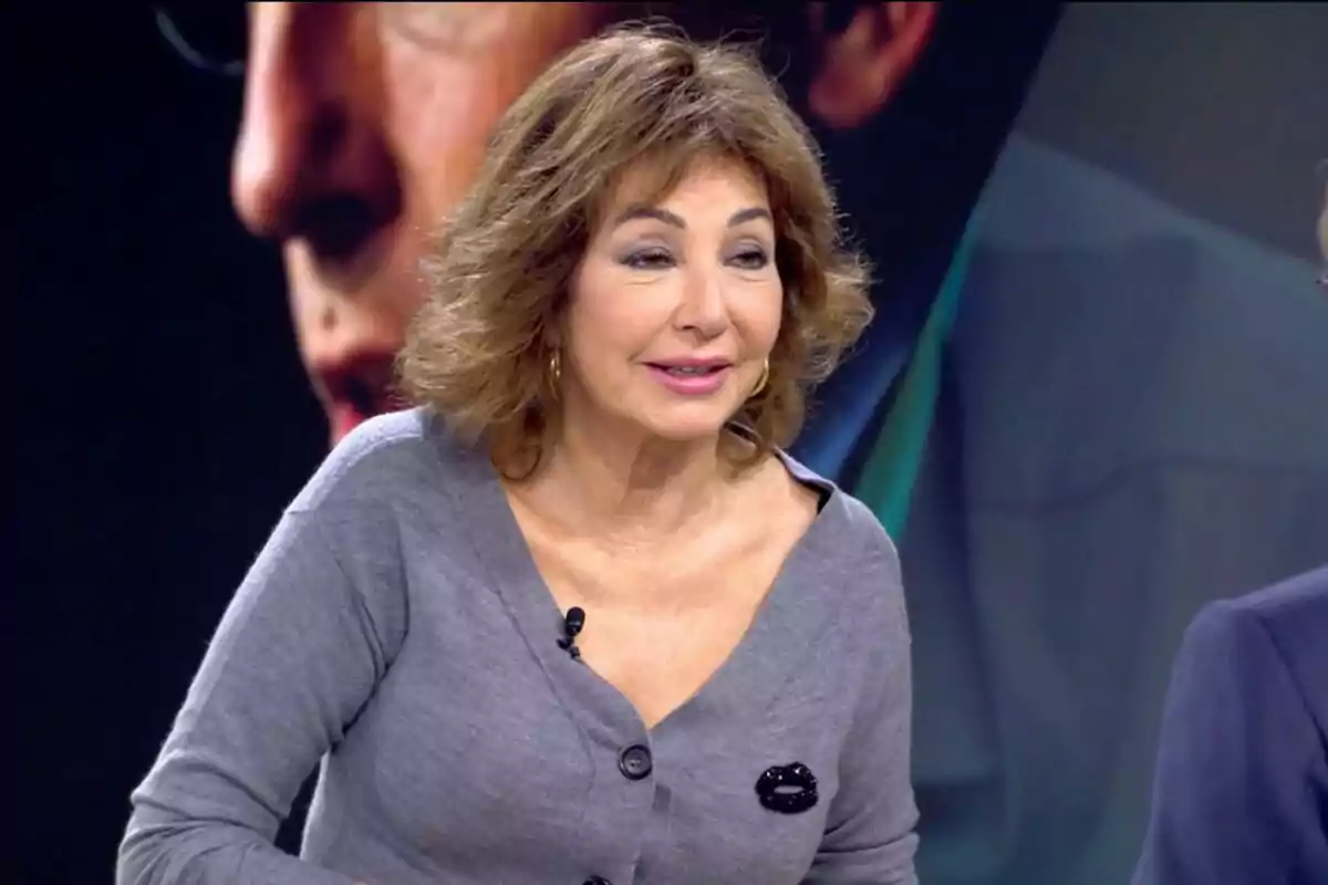 Una mujer con cabello castaño y rizado lleva un suéter gris y está en un estudio de televisión. Una mujer con cabello castaño y rizado lleva un suéter gris y está en un estudio de televisión.