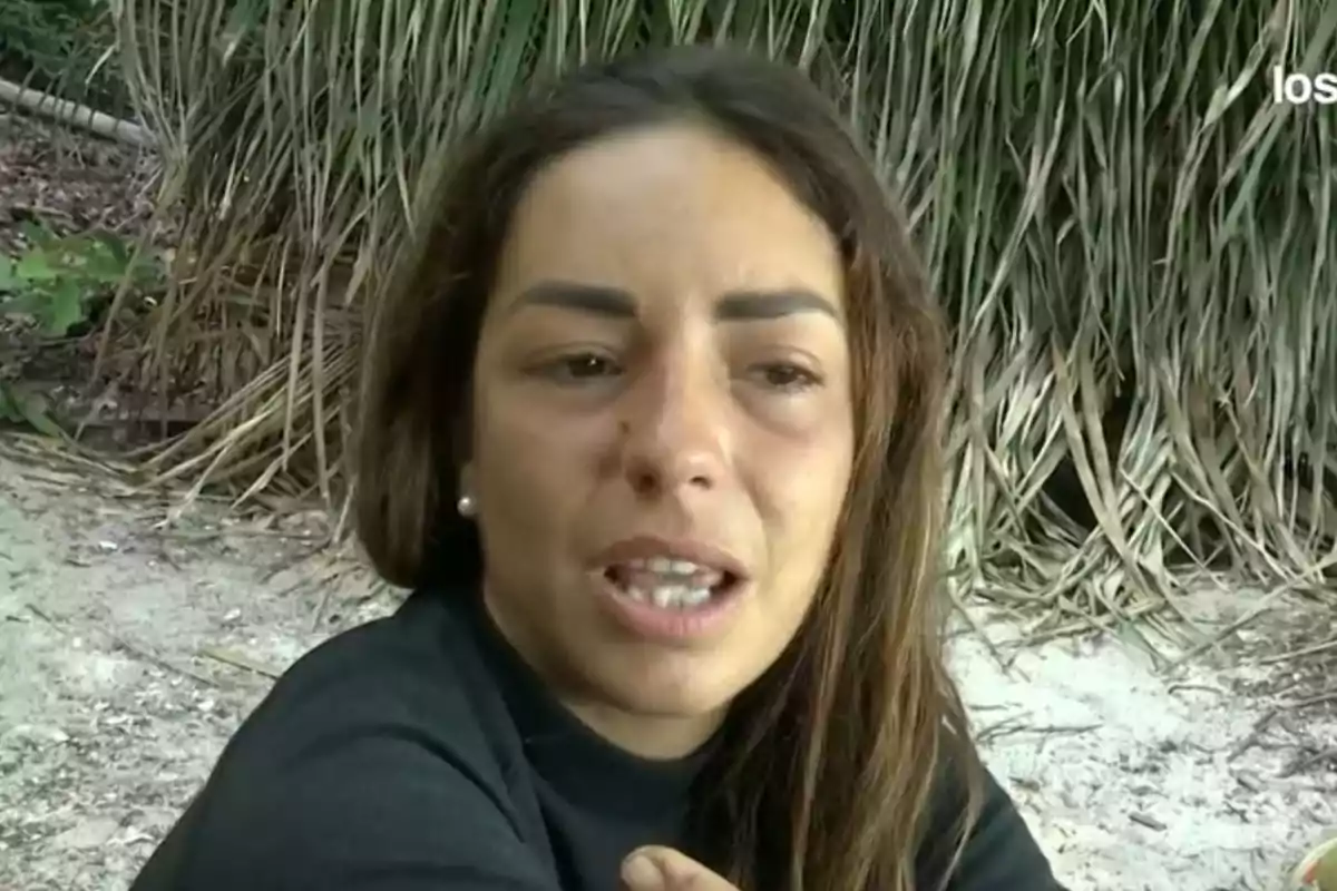 Anita Williams con expresión seria está sentada en una playa con vegetación de fondo. Anita Williams con expresión seria está sentada en una playa con vegetación de fondo.