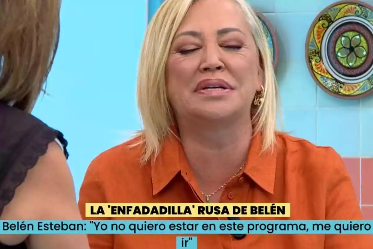 Belén Esteban con cabello rubio y camisa naranja aparece en un programa de televisión, con los ojos cerrados y una expresión facial que sugiere frustración o descontento. Belén Esteban con cabello rubio y camisa naranja aparece en un programa de televisión, con los ojos cerrados y una expresión facial que sugiere frustración o descontento.