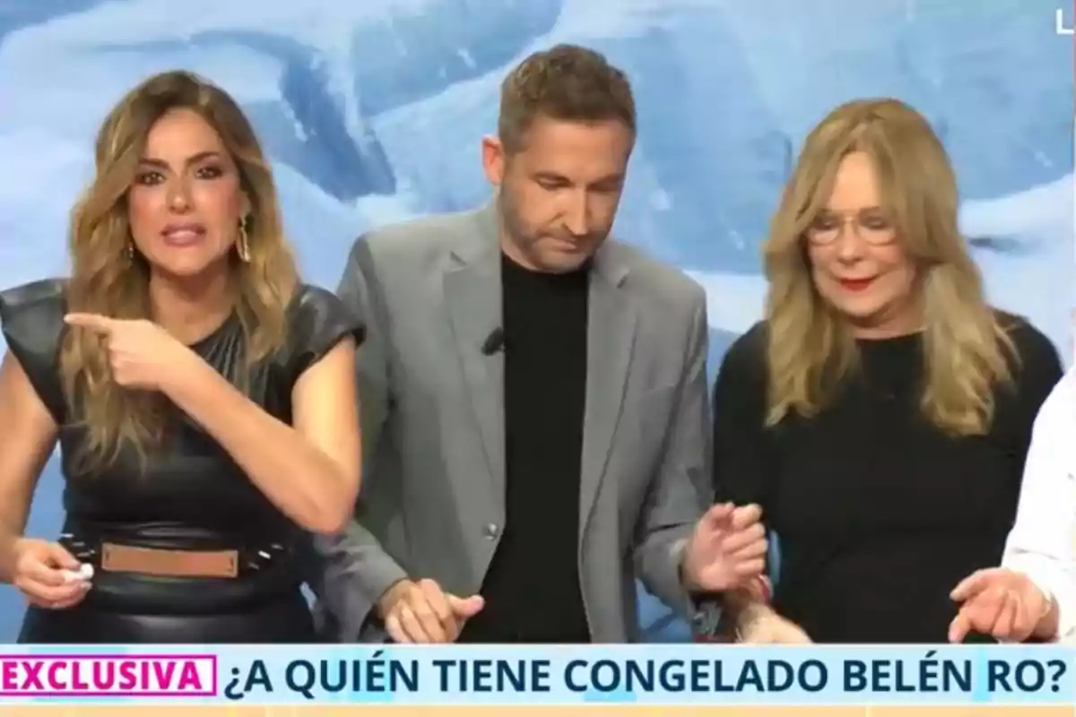 Tres personas están en un set de televisión, Verónica Dulanto a la izquierda señala hacia un lado mientras Frank Blanco en el centro y Belén Rodríguez a la derecha miran hacia abajo, en la parte inferior de la imagen hay un texto que dice Tres personas están en un set de televisión, Verónica Dulanto a la izquierda señala hacia un lado mientras Frank Blanco en el centro y Belén Rodríguez a la derecha miran hacia abajo, en la parte inferior de la imagen hay un texto que dice