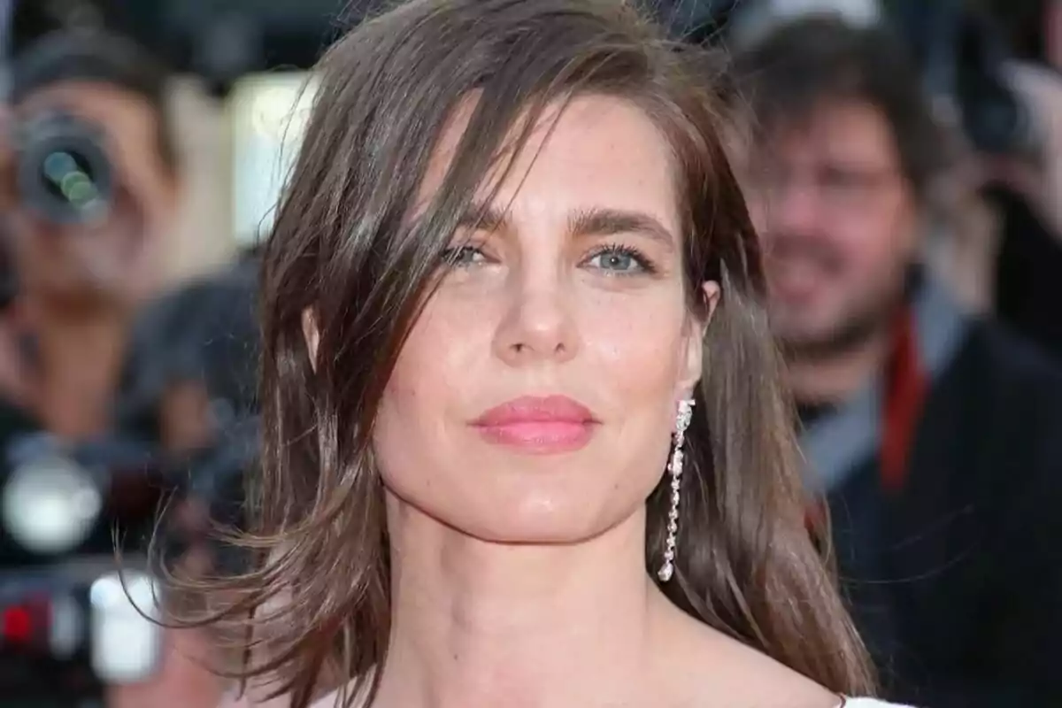 A person with brown hair and a long earring posing in front of cameras at an event. A person with brown hair and a long earring posing in front of cameras at an event.