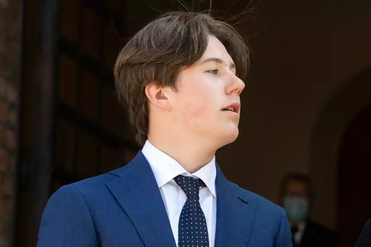 A young man in a blue suit and a white polka dot tie looks to the side. A young man in a blue suit and a white polka dot tie looks to the side.