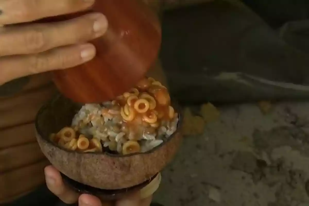 Persona sirviendo espaguetis en salsa de tomate sobre arroz en un cuenco hecho de coco Persona sirviendo espaguetis en salsa de tomate sobre arroz en un cuenco hecho de coco