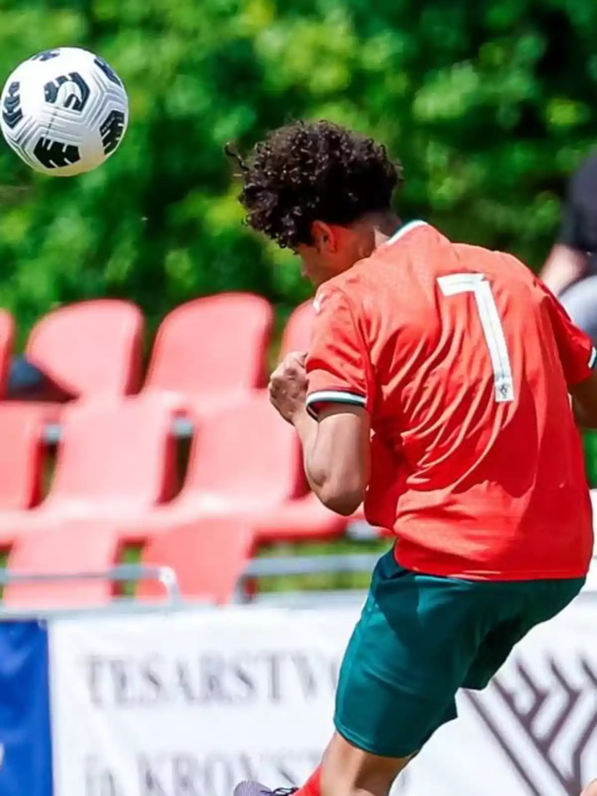Soccer player with a red jersey and number seven heads a ball on a field with red seats and a green background. Soccer player with a red jersey and number seven heads a ball on a field with red seats and a green background.