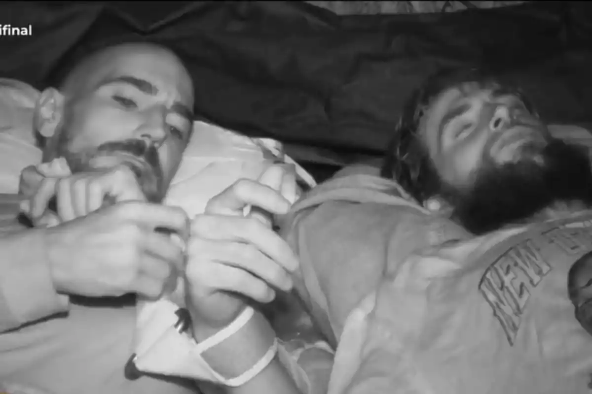 Damián y Montoya acostados uno de ellos con los ojos cerrados y el otro mirando hacia el frente en una escena en blanco y negro Damián y Montoya acostados uno de ellos con los ojos cerrados y el otro mirando hacia el frente en una escena en blanco y negro