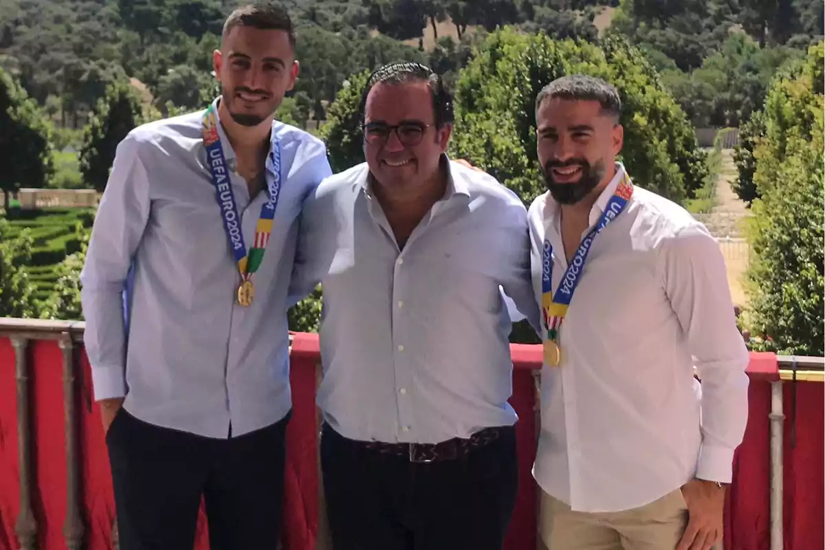 Tres hombres posan juntos al aire libre, dos de ellos llevan medallas de la UEFA EURO 2020 alrededor del cuello.