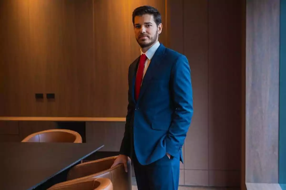 Hombre de pie en una sala de reuniones vistiendo un traje azul y corbata roja.