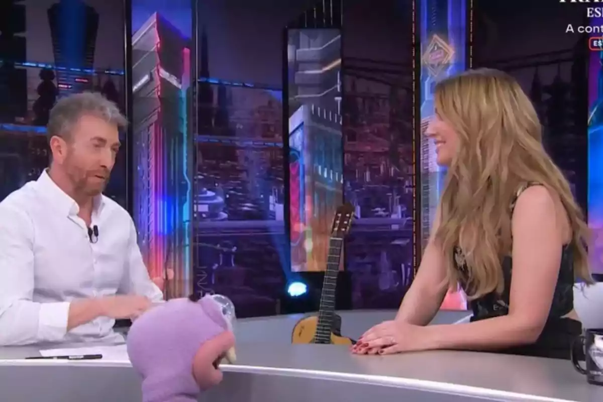 Pablo Motos y Edurne conversan en un set de televisión con un fondo colorido y una guitarra apoyada detrás de ellos, mientras un personaje de peluche está en primer plano. Pablo Motos y Edurne conversan en un set de televisión con un fondo colorido y una guitarra apoyada detrás de ellos, mientras un personaje de peluche está en primer plano.